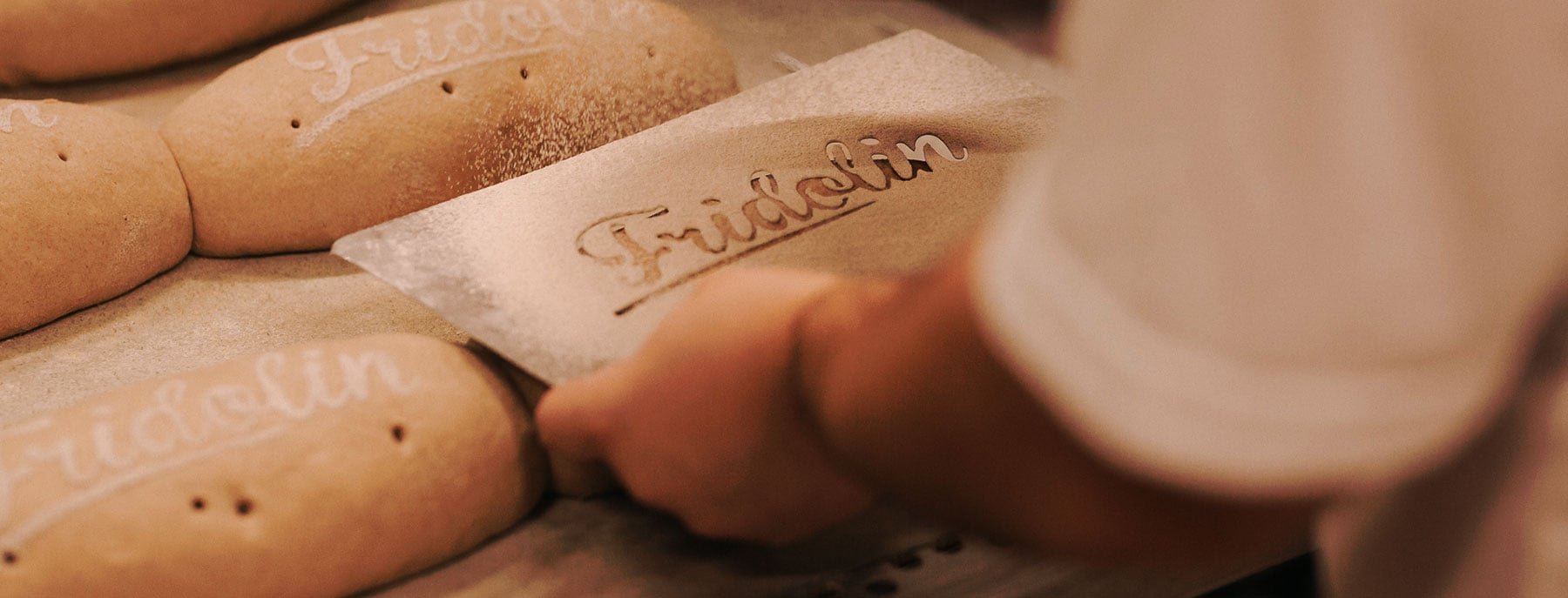 Ein Bäcker schreibt mit einer Schablone und Mehl den Namen Fridolin auf Brote